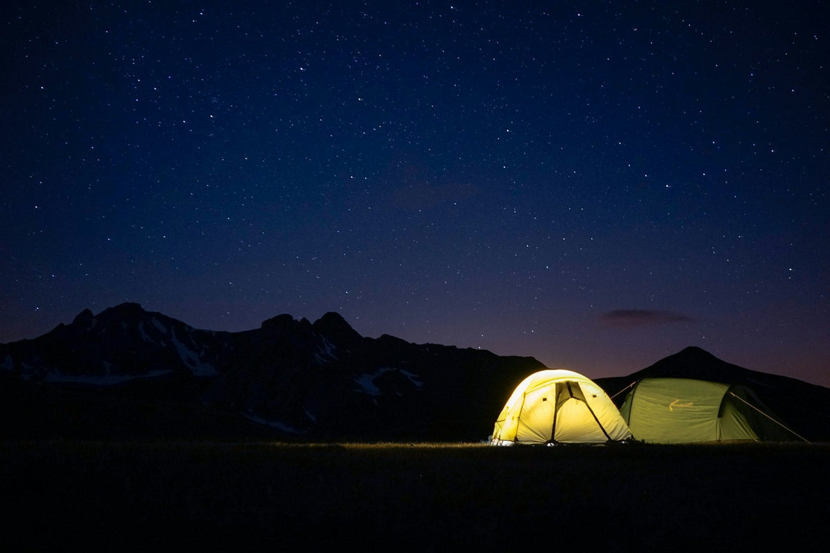 Tents glowing with light below mountains at night