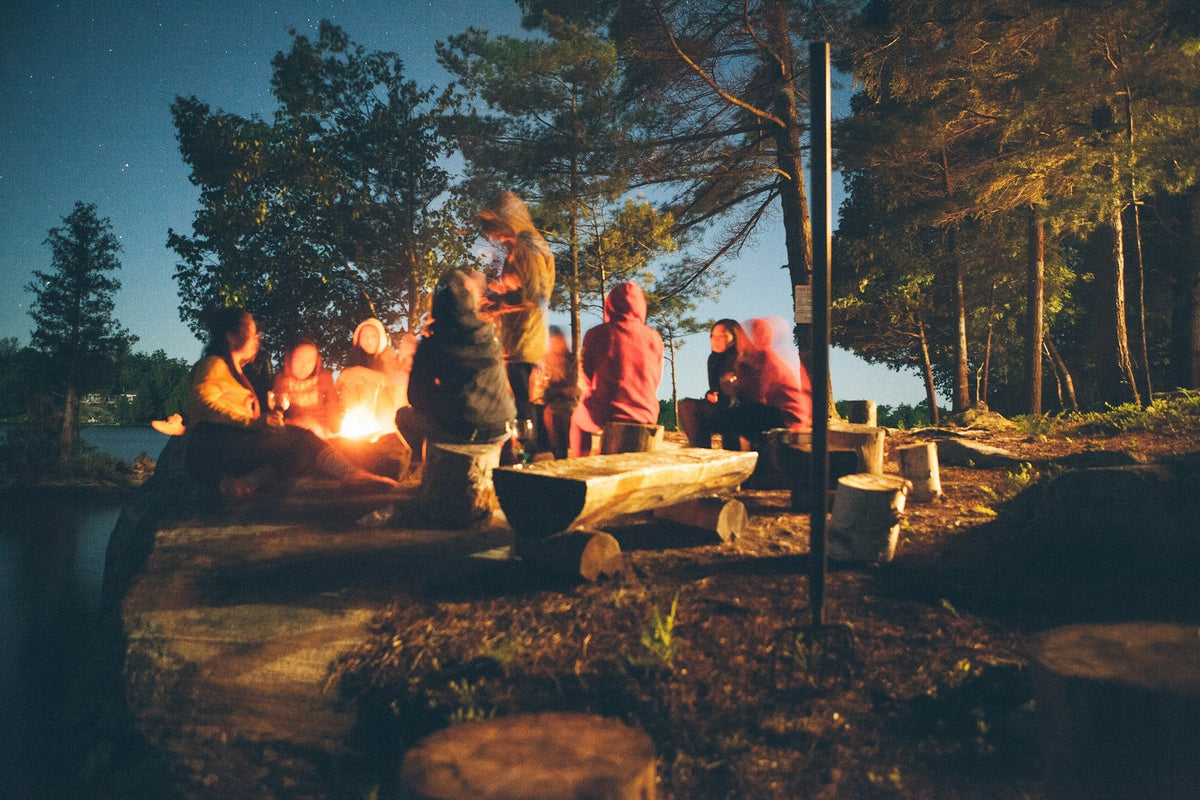 Friends gathered around a campfire at a lakeside campsite