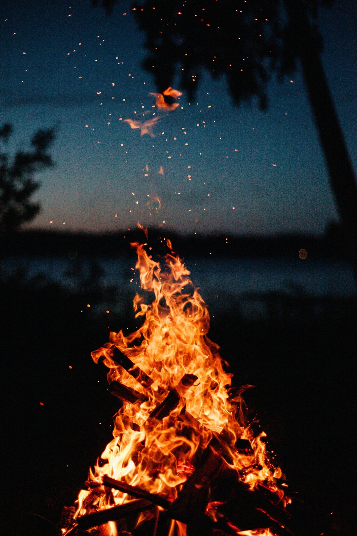 Bright campfire flames with sparks rising into the night