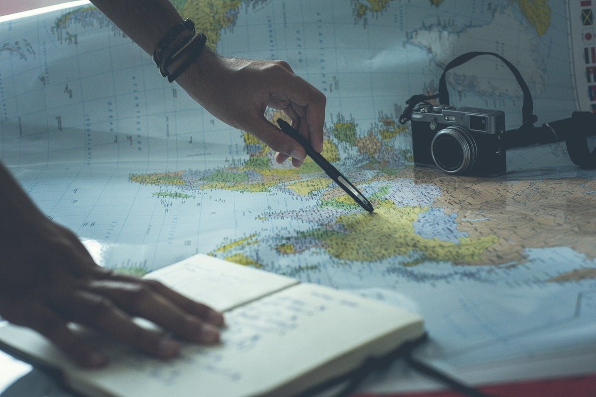 Hands planning a route on a paper map with a pencil and notebook