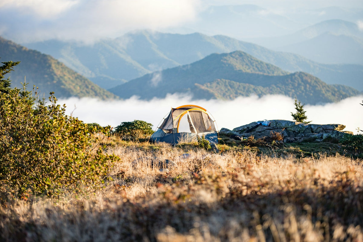 Tent pitched on a grassy ridge above a sea of clouds and mountains