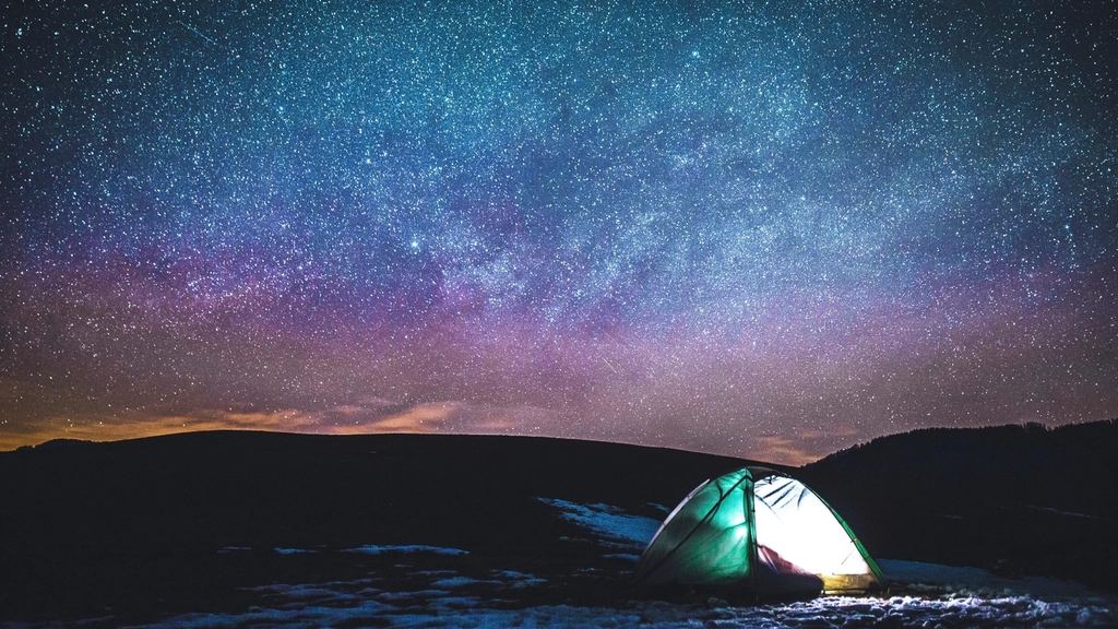Tent glowing under the Milky Way on a mountain ridge